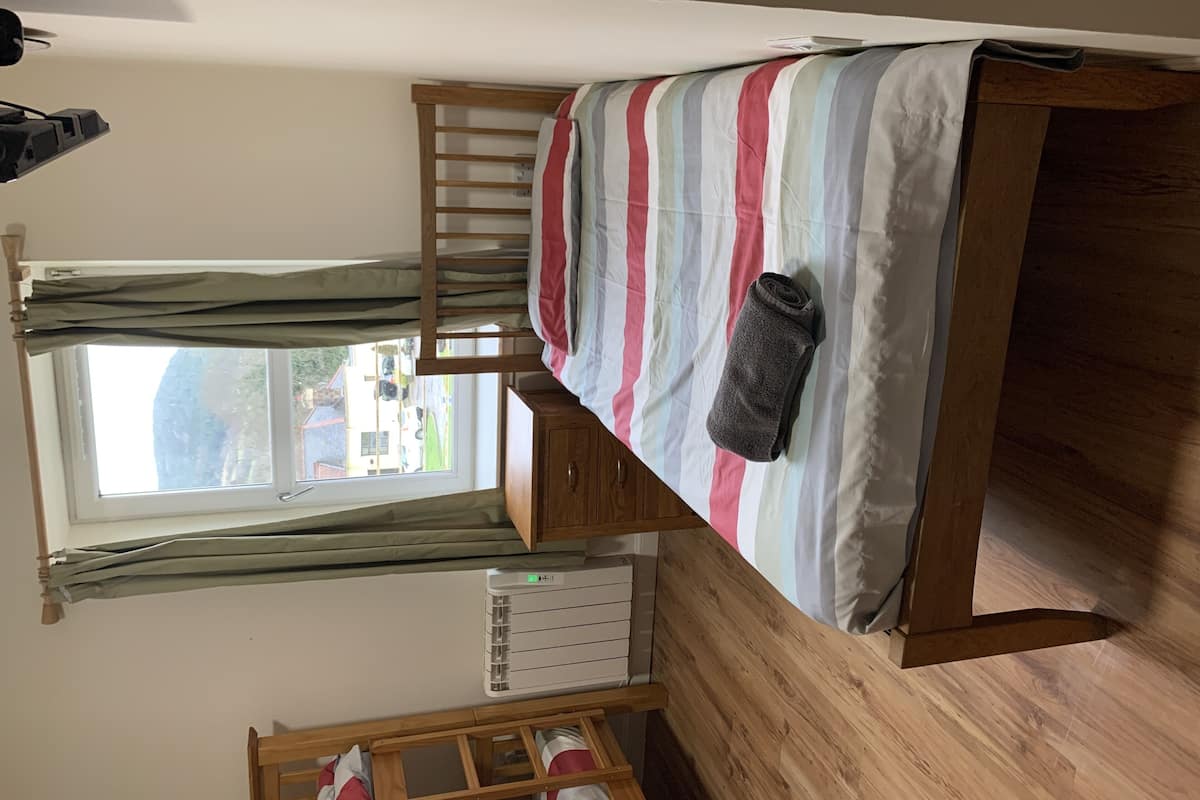 A bunk bed with a striped bedspread, a rolled-up towel, and a window with curtains.