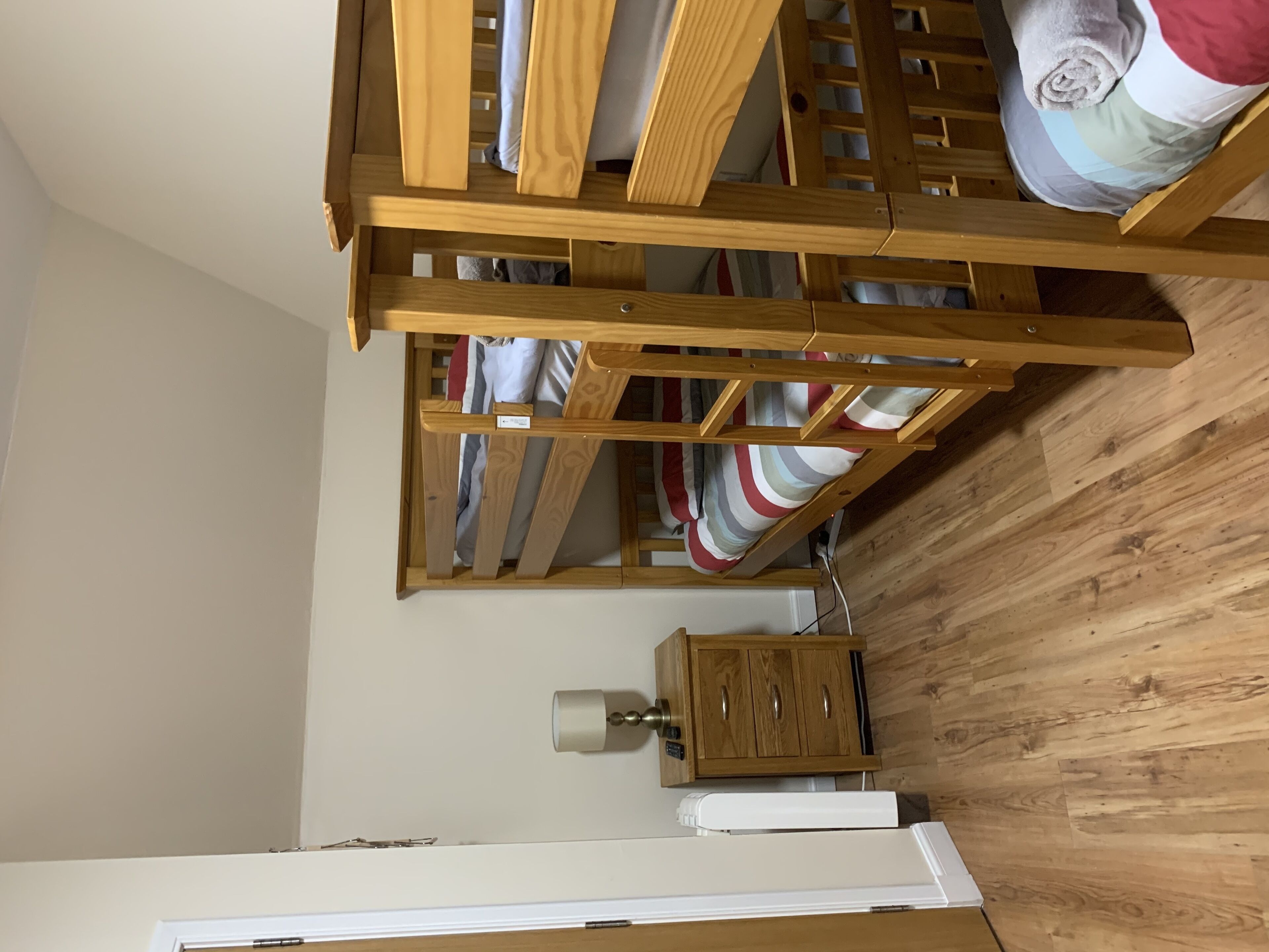 A room with a wooden bunk bed, a wooden cabinet, and a white bedside table.