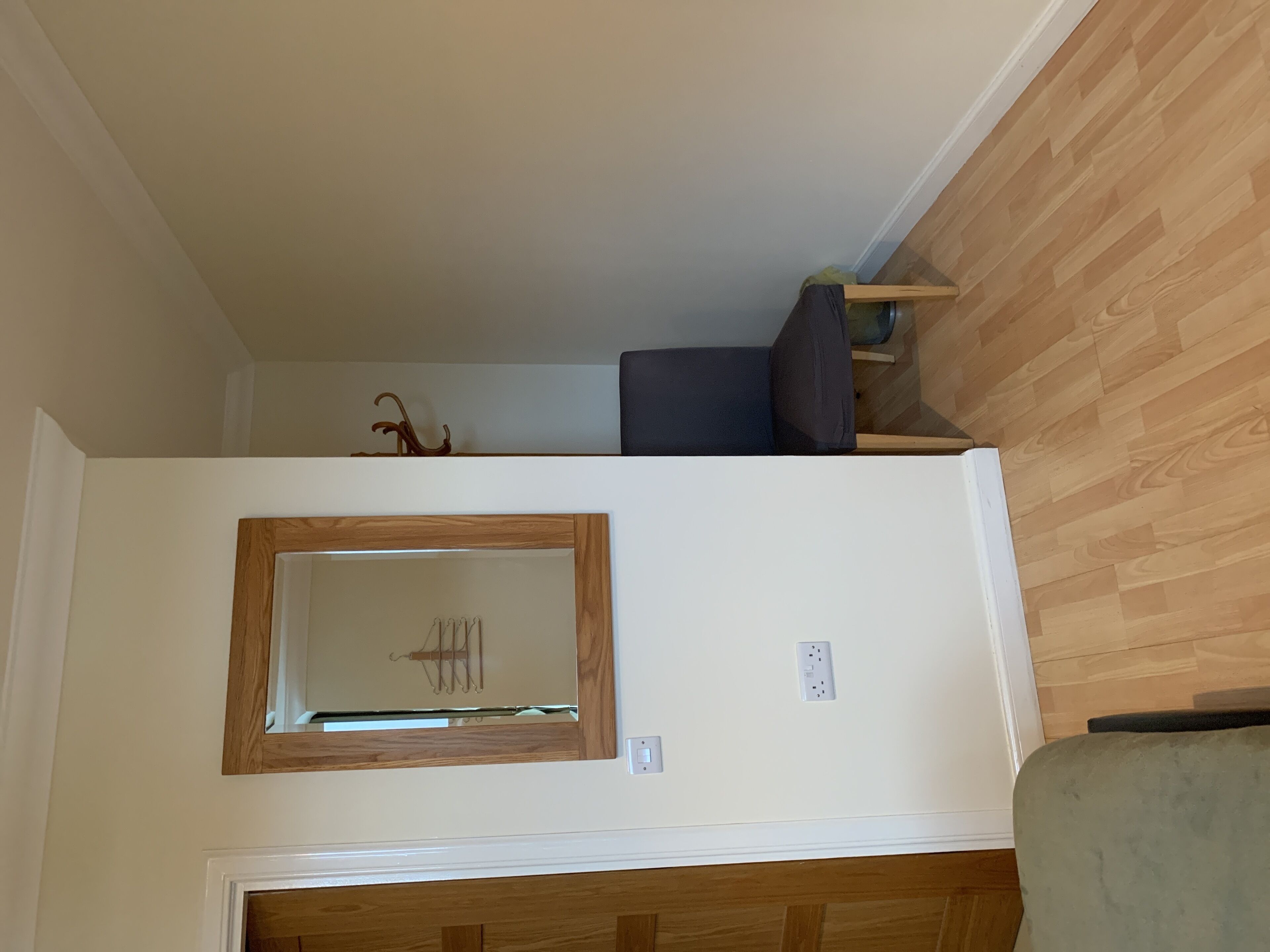 A room with a wooden floor, a white wall, a mirror, and a door.