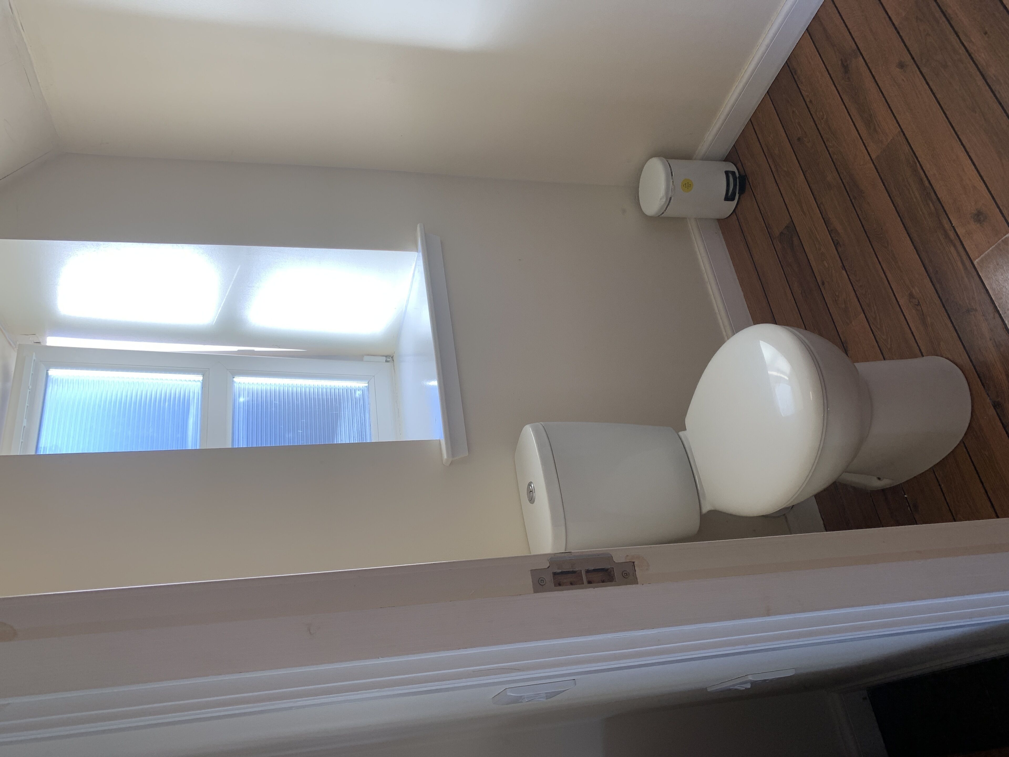 A bathroom with a toilet, a window, and a white wall.