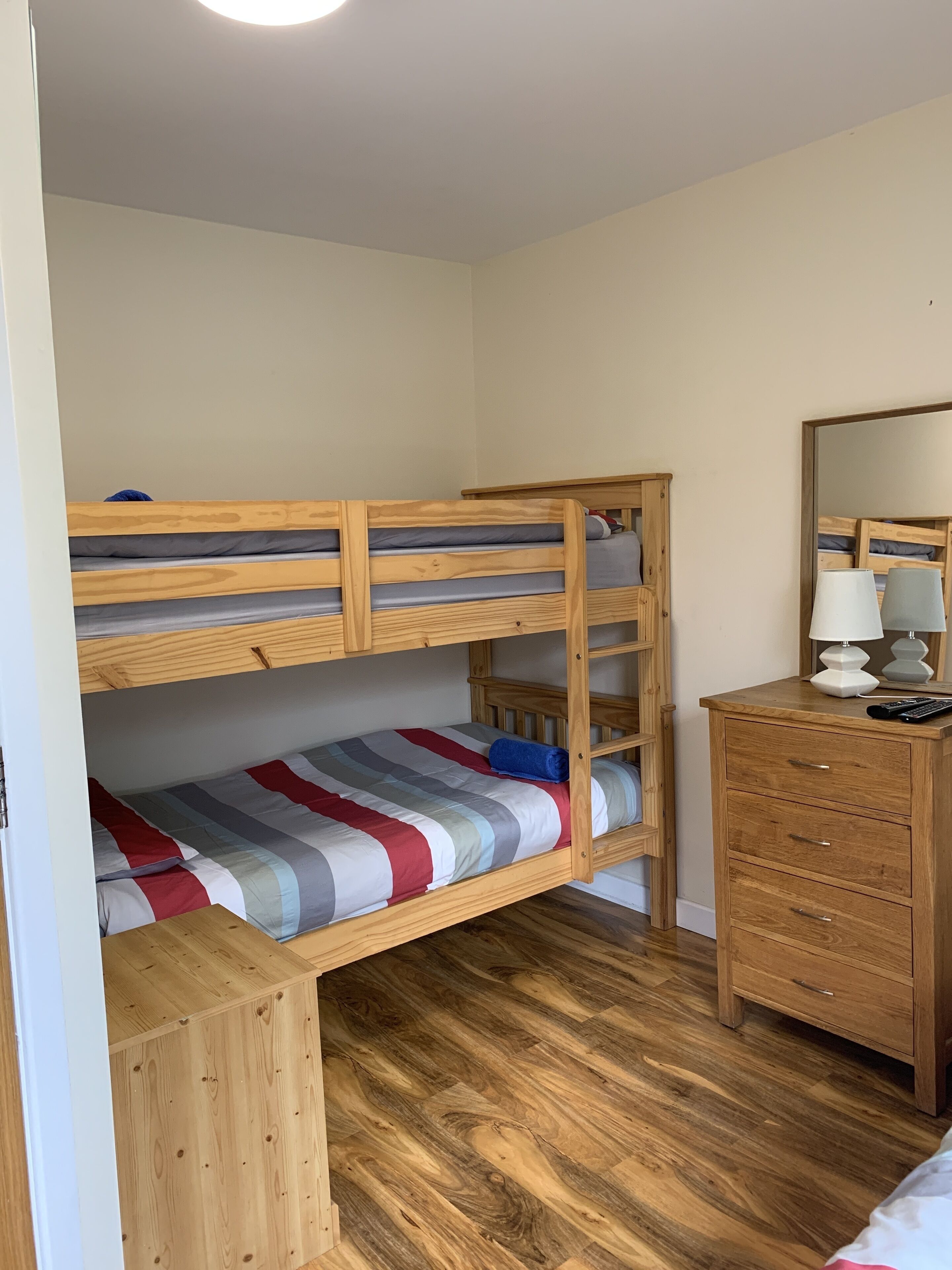 A bunk bed with a wooden frame, a dresser with drawers, and a mirror.