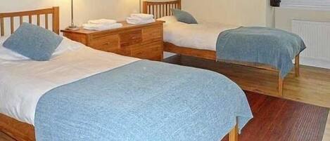 A room with two single beds, wooden headboards, bedside tables with lamps, and a view of the outdoors through a window.
