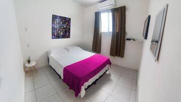 Un dormitorio con una cama, una mesita con una planta, un cartel en la pared y un equipo de aire acondicionado.