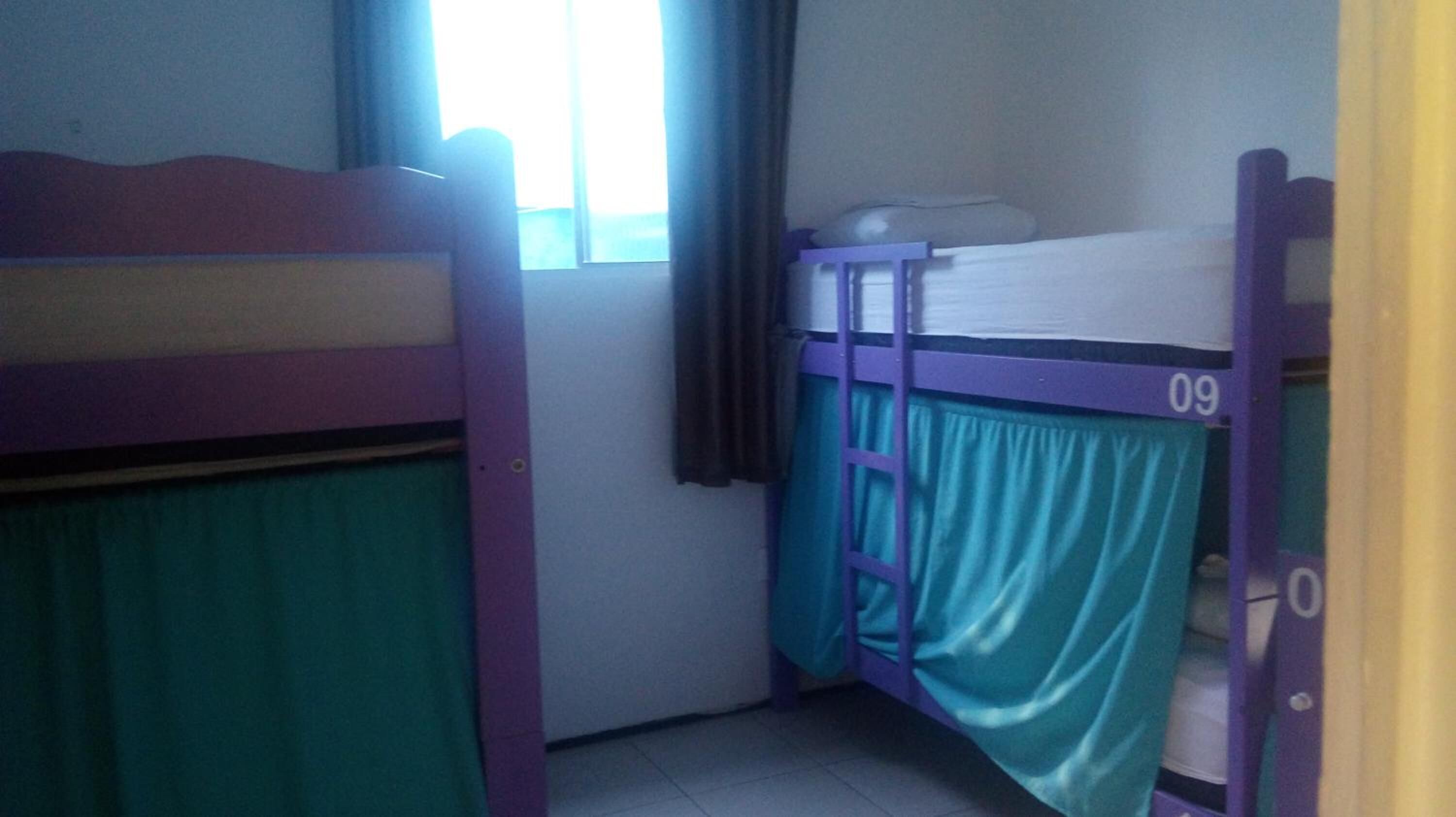 Um quarto com duas beliches, uma com cortina verde e a outra com cortina azul.