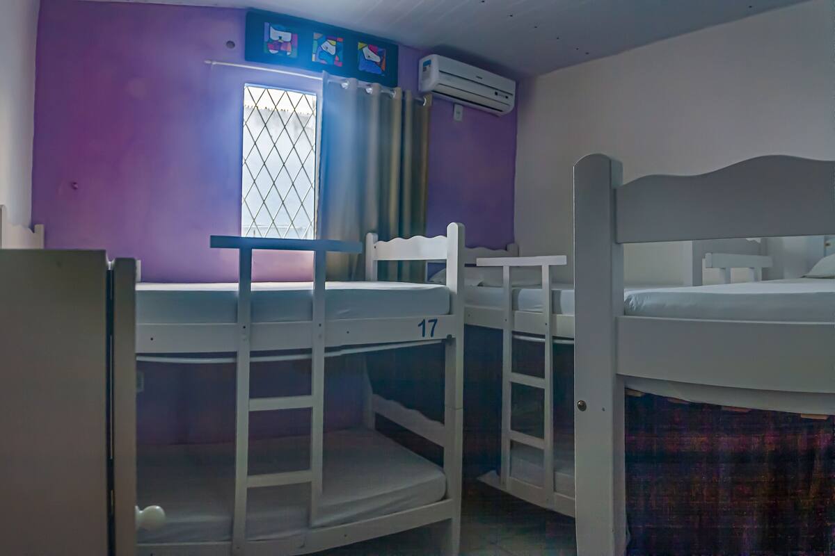 Ein Zimmer mit Etagenbetten, einem Vorhangfenster, einer Klimaanlage und einer violetten Wand.