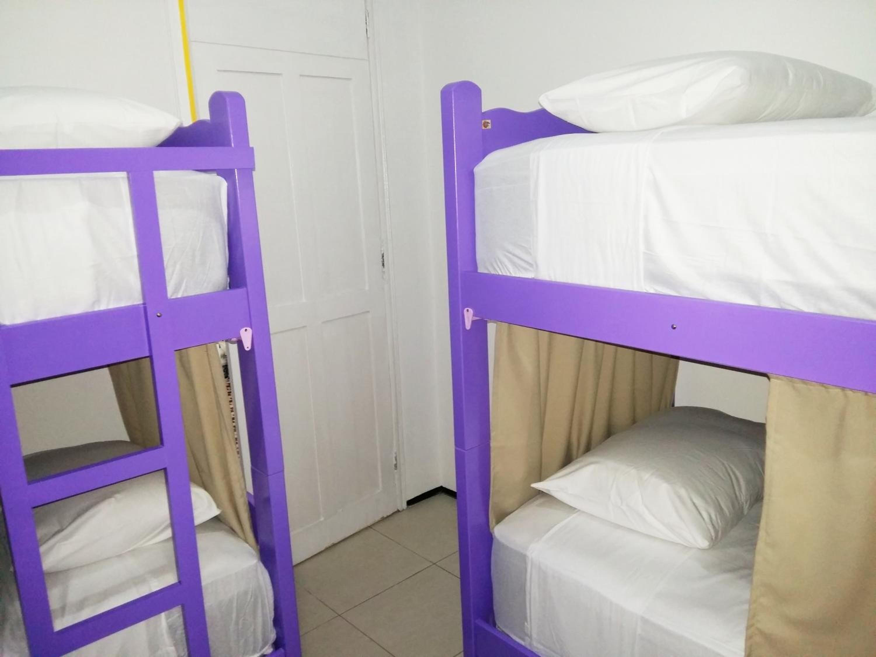 Two bunk beds with white bedding and purple frames in a room with a white door and tiled floor.