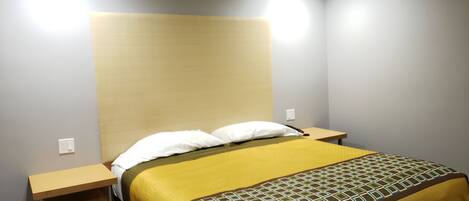 Une chambre d’hôtel avec un lit, deux tables de chevet et une tête de lit.
