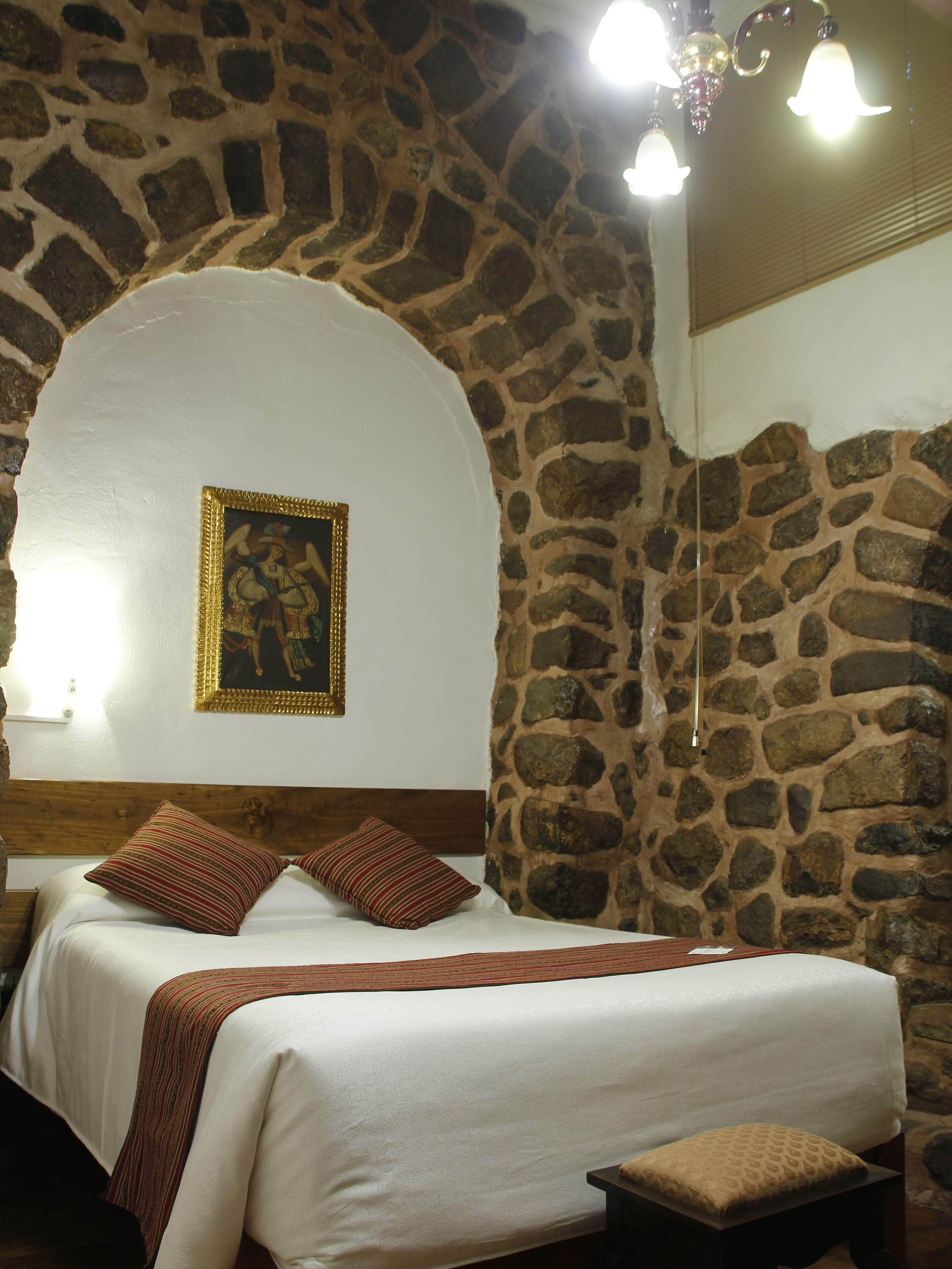 Una cama con cabecera, una pared de piedra y un cuadro enmarcado en la pared.