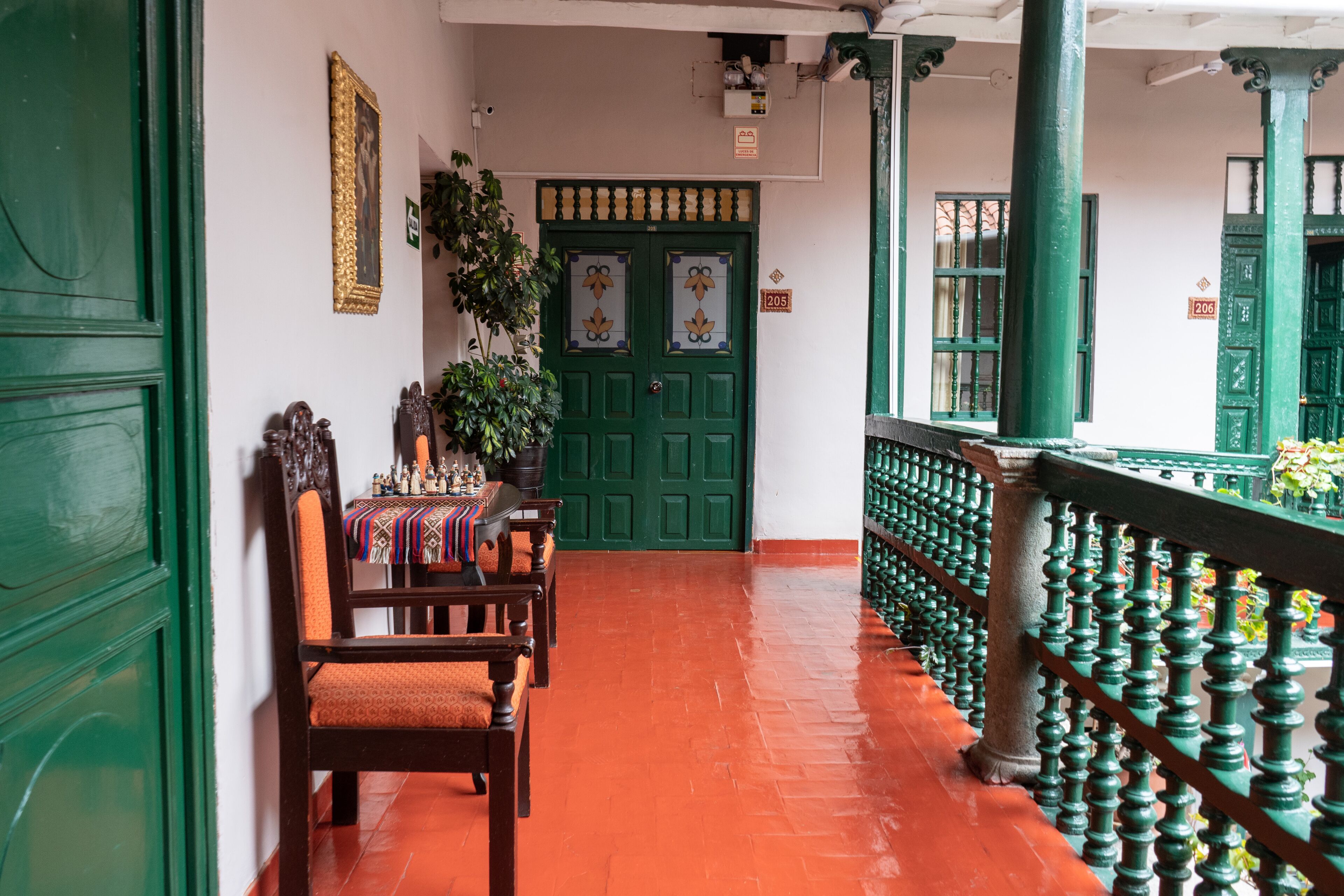 A corridor with green doors, wooden chairs, and a tiled floor.