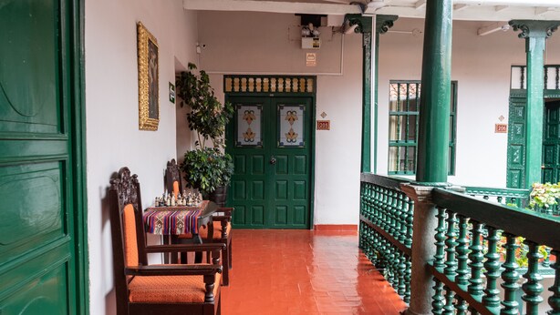 A corridor with green doors, wooden chairs, and a tiled floor. - La Casona Real (Cusco)