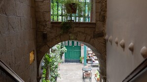 Un arco de piedra que da a un patio con una puerta verde, plantas en macetas y mobiliario exterior.