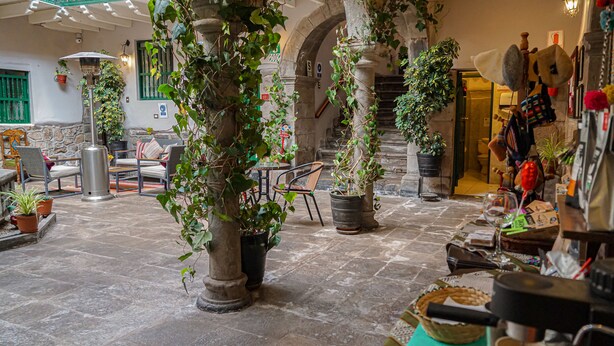 Un patio con suelo de piedra, plantas en macetas, mobiliario exterior y una escalera que lleva a un nivel superior.