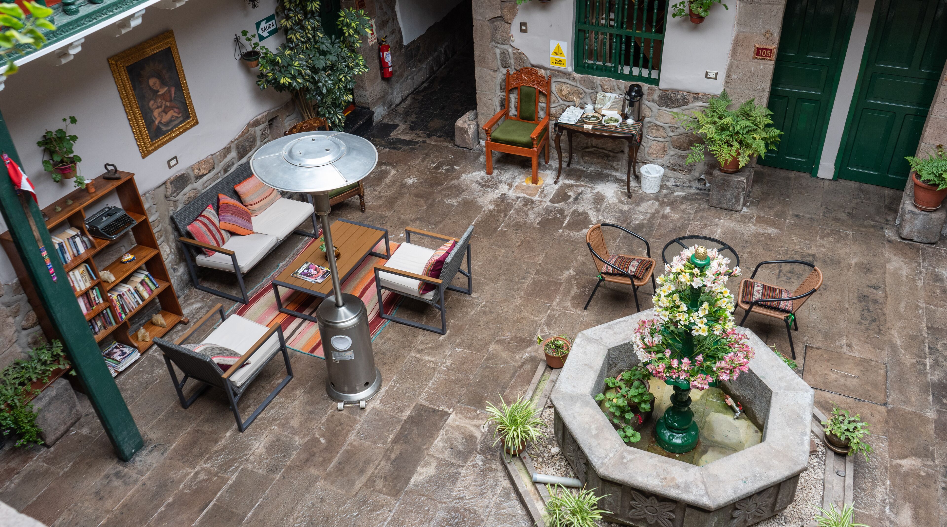 A courtyard with a seating area, a bookshelf, a table with a kettle, and a water feature.