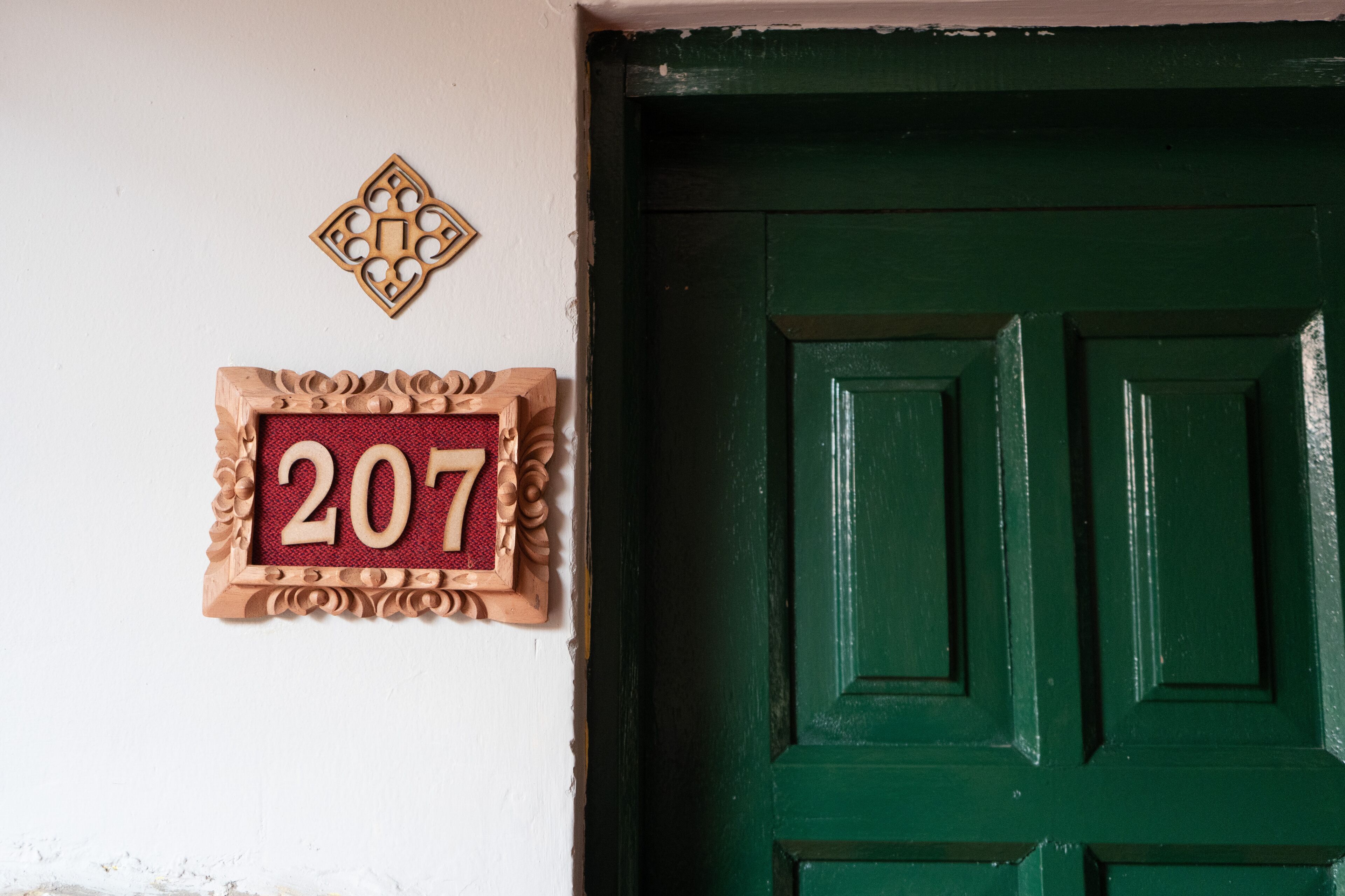 A green door with a wooden number plaque displaying '207' on a white wall.