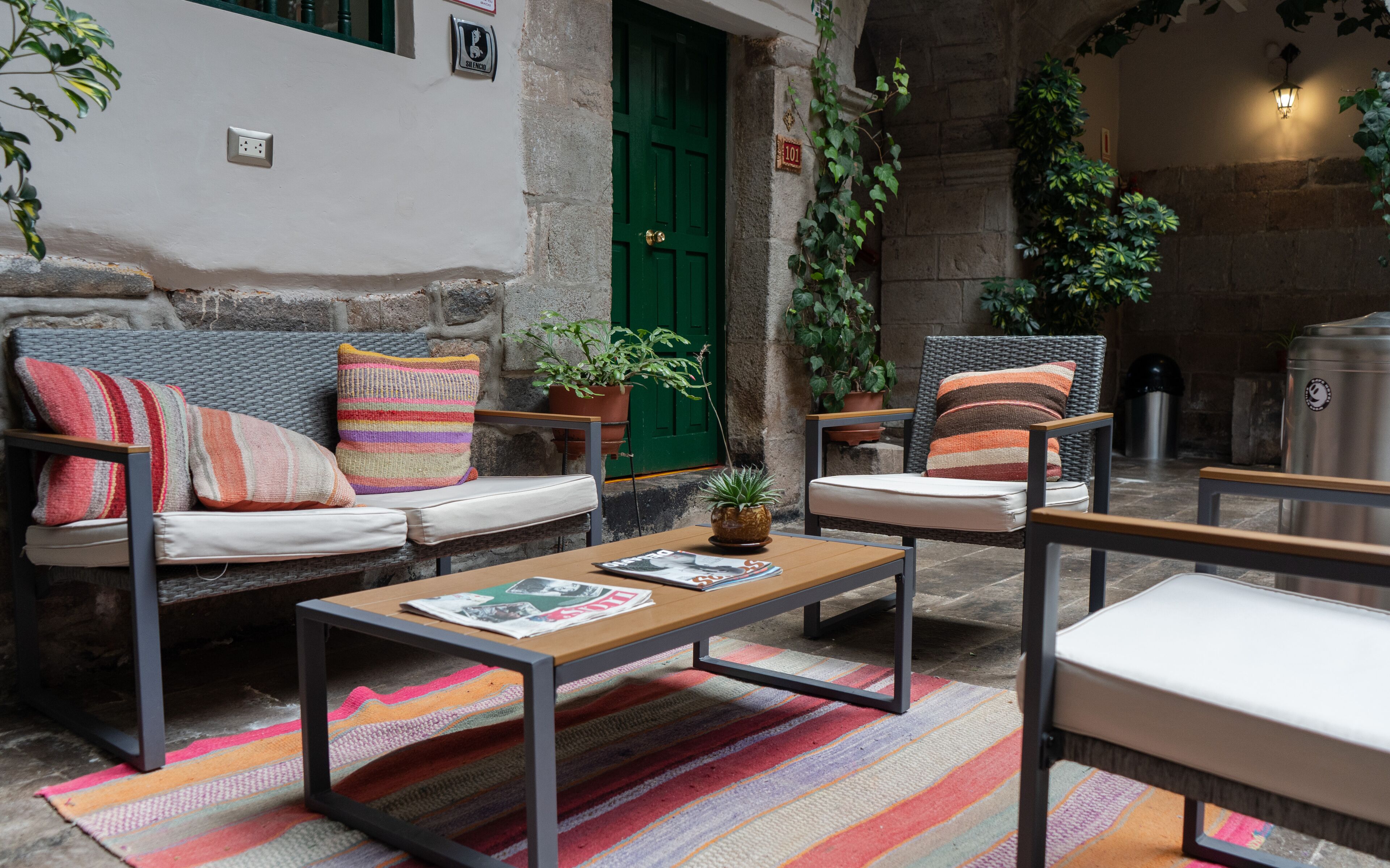 Un área de estar al aire libre acogedora, con un sofá, sillas, una mesa de madera y un colorido tapete a rayas.