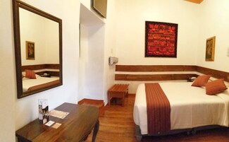 Una habitación de hotel con cama, escritorio, espejo y una obra de arte colgada en la pared.