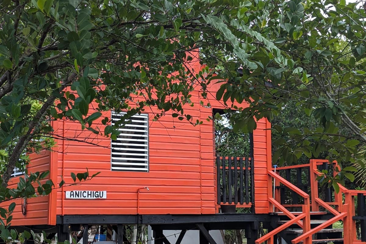 Un bâtiment rouge avec une enseigne sur laquelle on peut lire « ANICHIGU » et une fenêtre équipée de stores horizontaux.