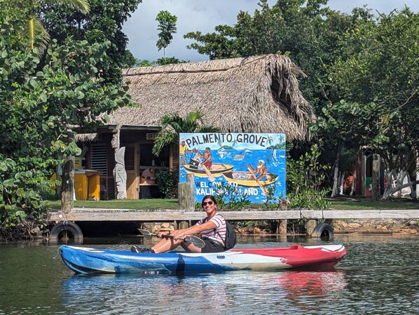 A man in a kayak on a river with a sign in the background that reads "Palmento Grove Welcome to Kalipata Island." - Palmento Grove Eco Cultural & Fishing Lodge (Hopkins)