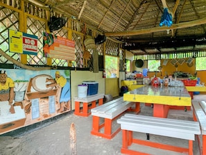 A rustic dining area with a thatched roof, wooden benches, and a mural depicting traditional activities. - Palmento Grove Eco Cultural & Fishing Lodge (Hopkins)