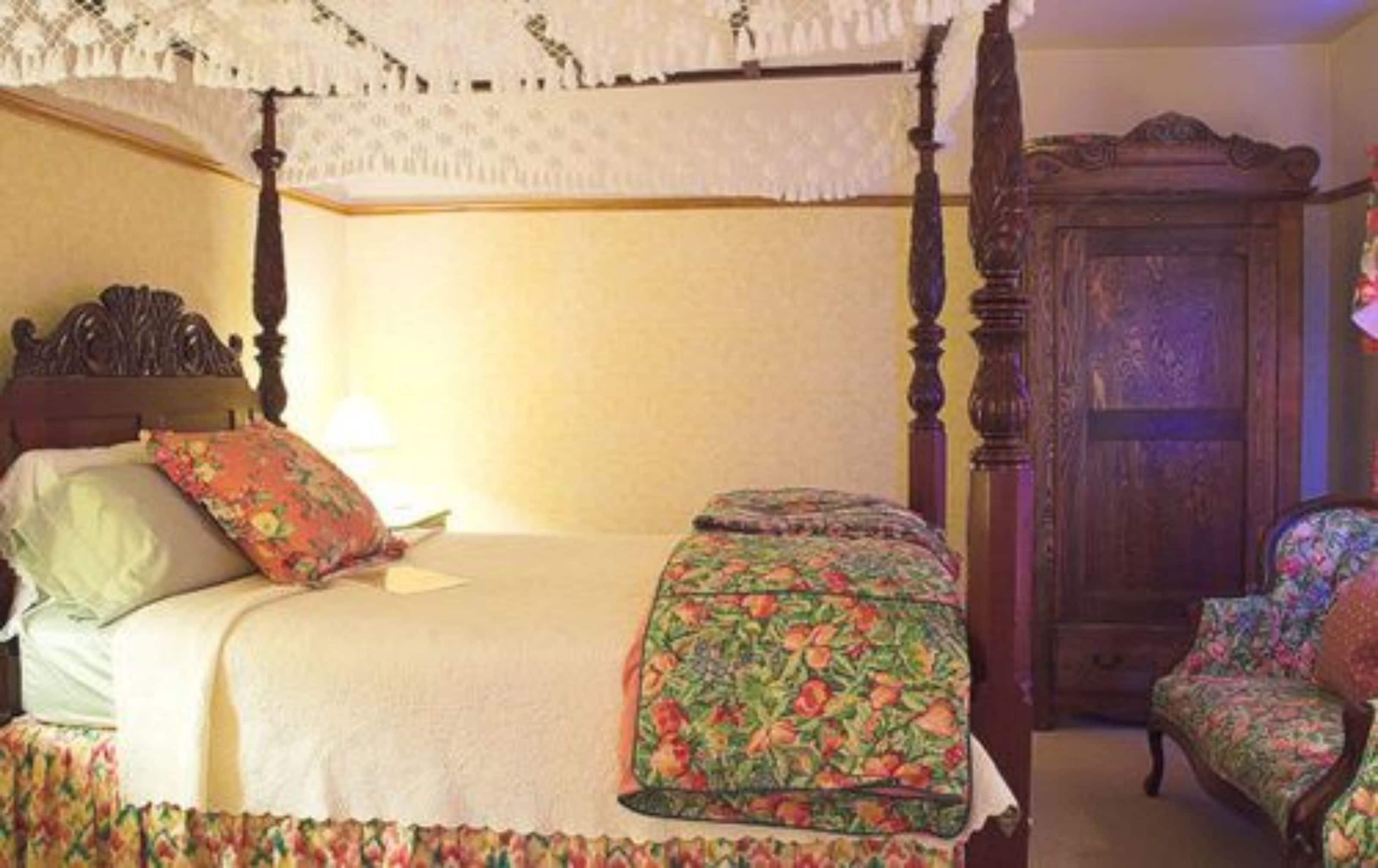A four-poster bed with floral bedding, a nightstand, and a wooden wardrobe.