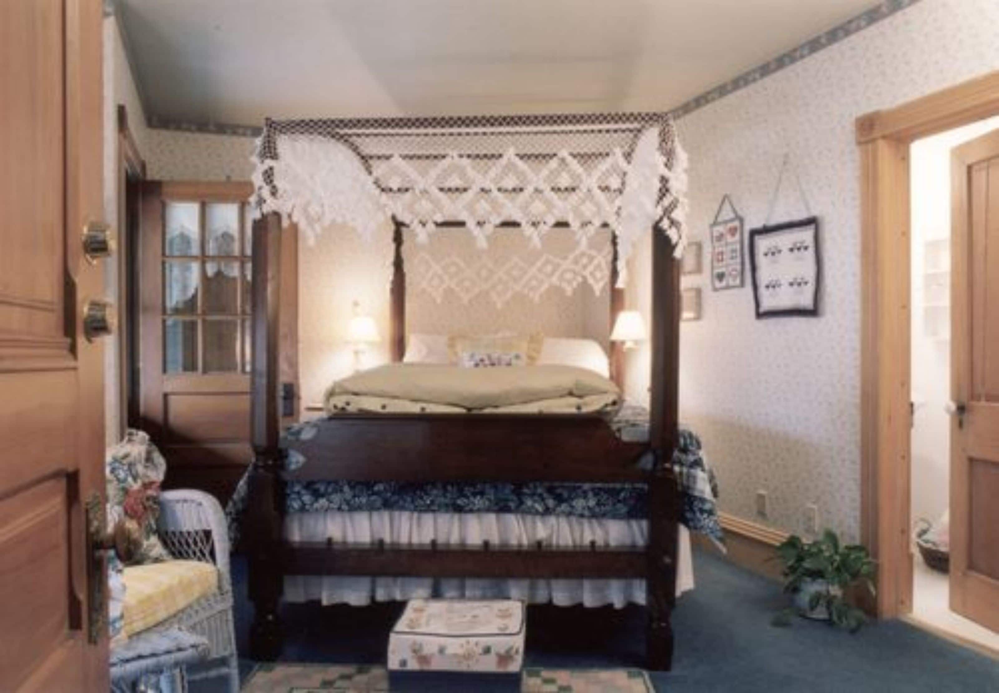 Una cama con dosel adornada con dosel de encaje, una mesita de noche, una silla y una pequeña mesita auxiliar.