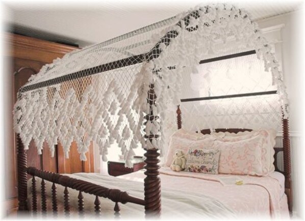 Un lit à baldaquin avec un ciel de lit en dentelle, une tête de lit en bois et un coussin à motifs floraux.