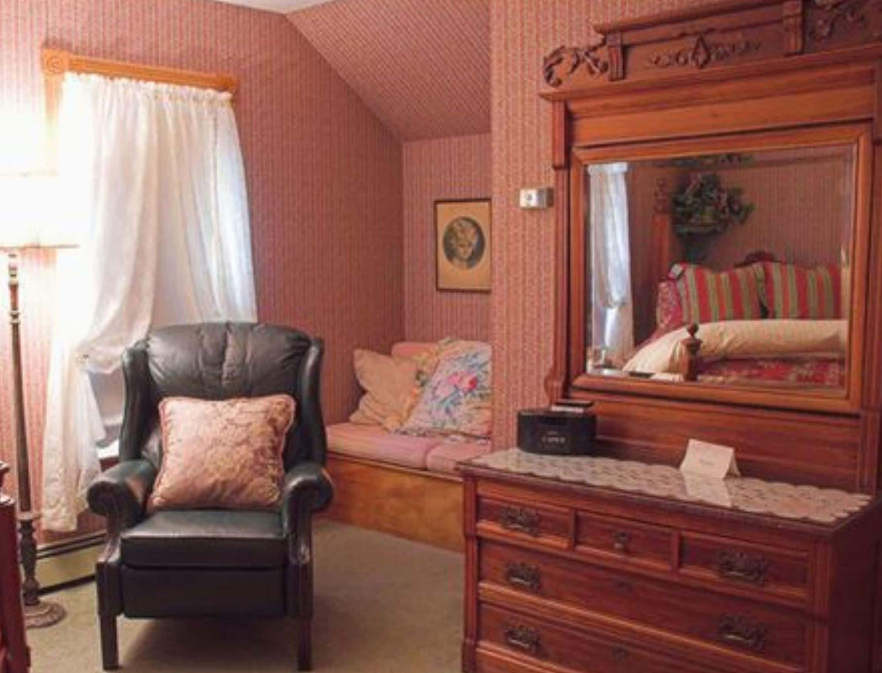 A cozy room with a black leather armchair, a wooden dresser, and a bed with striped bedding.