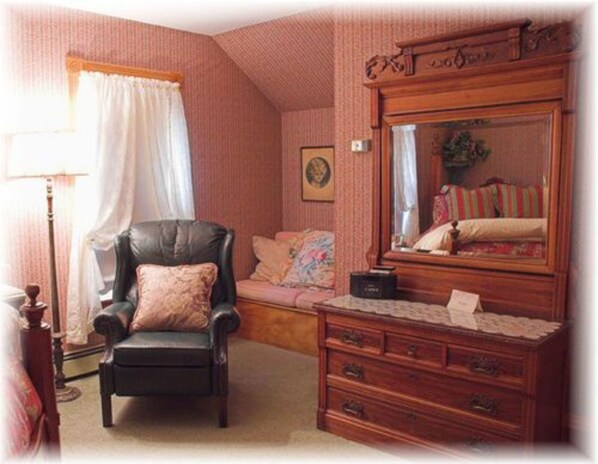 A room with a large wooden dresser, a black leather chair, a pink sofa, and a mirror reflecting the room's interior.