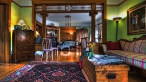 A traditional room with a wooden floor, a patterned rug, a sofa, a wooden chest, and a chair. - White Lace Inn (Sturgeon Bay)