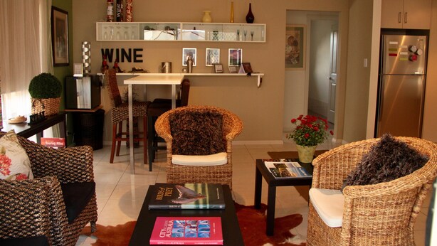 A living room with wicker furniture, a dining table, and a bookshelf with wine-themed decor. - Vintners House (McLaren Vale)