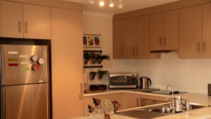 A modern kitchen with stainless steel appliances, wooden cabinets, and decorative wall art. - Vintners House (McLaren Vale)