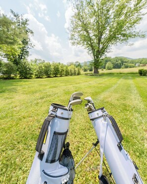 A golf bag with clubs on a grassy field with trees and a clear sky.