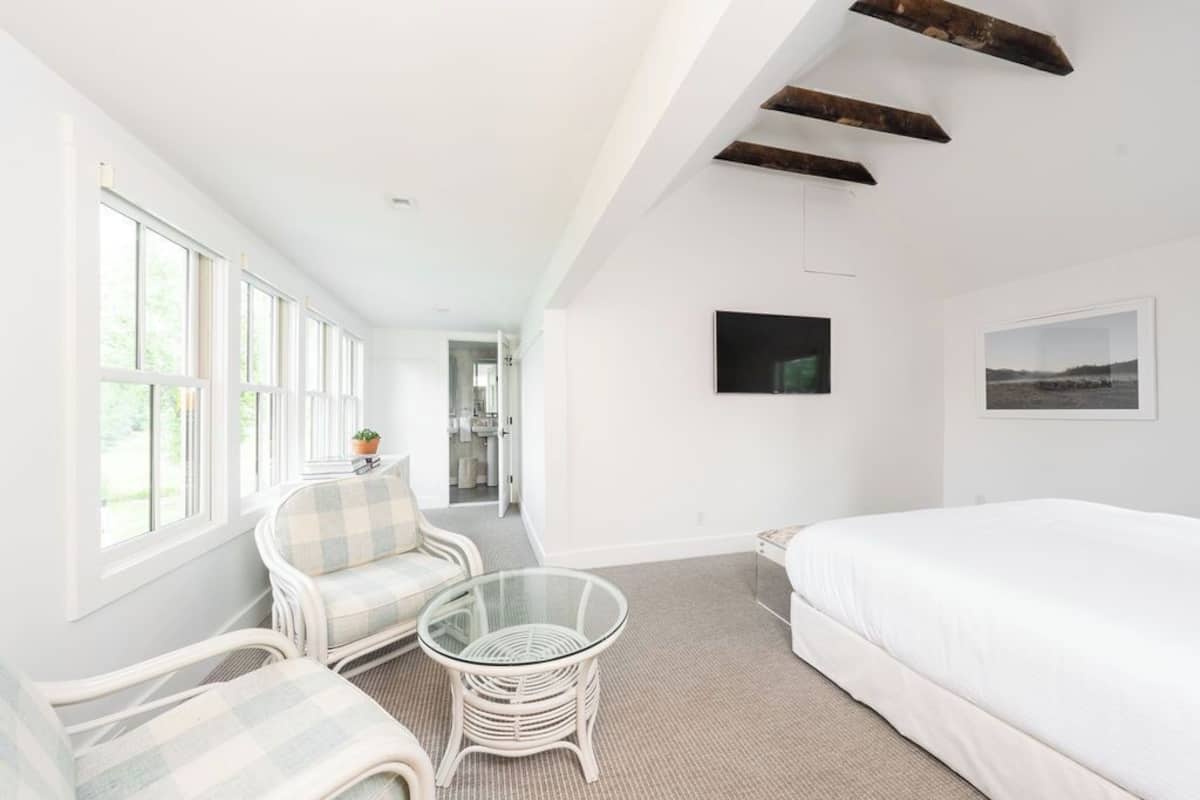 Una habitación amplia con una cama grande, una mesa de vidrio y un sofá. Cuenta con ventanas grandes y vistas al exterior.