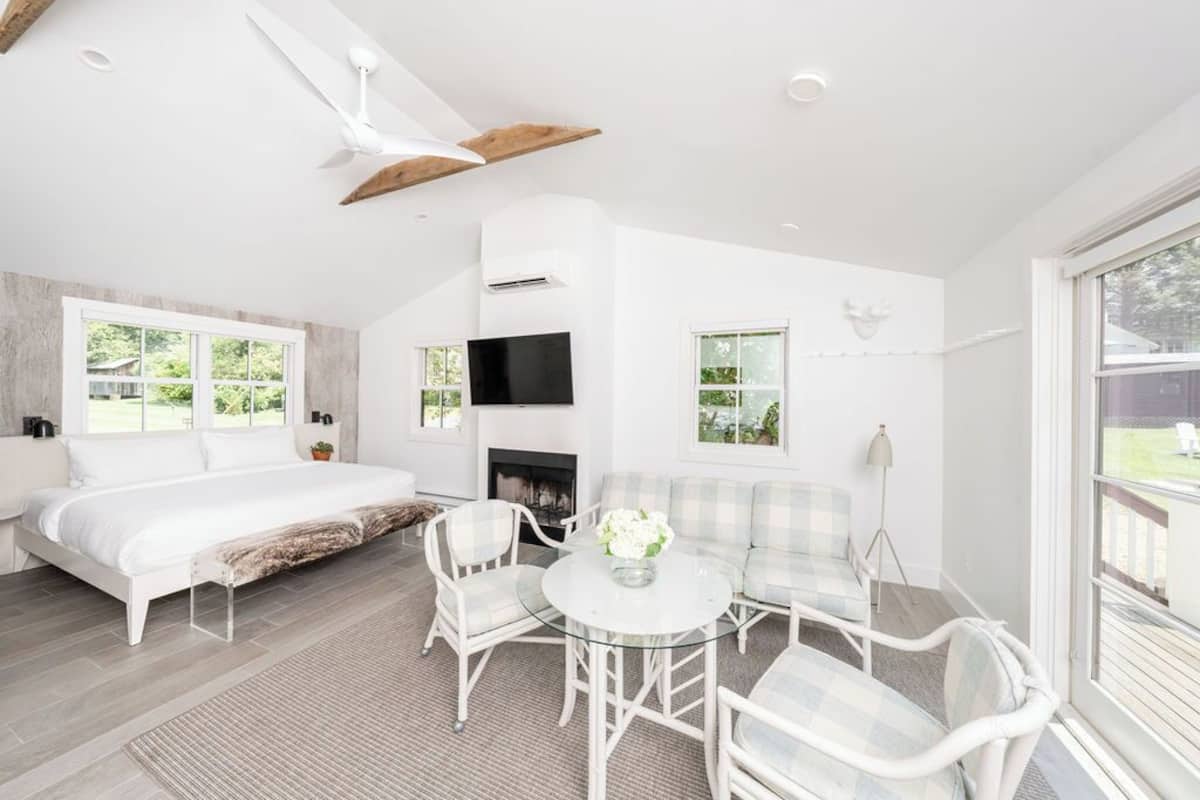 Un dormitorio moderno con cama, un rincón de descanso con mesa de vidrio y chimenea.