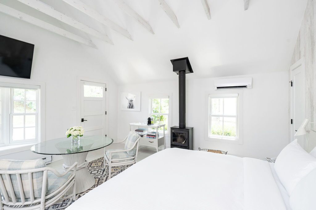 Una habitación blanca con una cama, una mesa con sillas, una chimenea y un televisor montado en la pared.