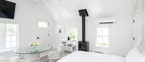 Una habitación blanca con una cama, una mesa con sillas, una chimenea y un televisor montado en la pared.