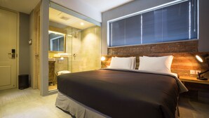Ein modernes Hotelzimmer mit einem großen Bett, einer Duschkabine aus Glas, einer Wand mit Ziegeln und einem Fenster mit Jalousien.