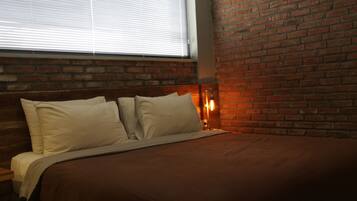 A bed with a brown bedspread and white pillows, a brick wall, and a window with blinds.