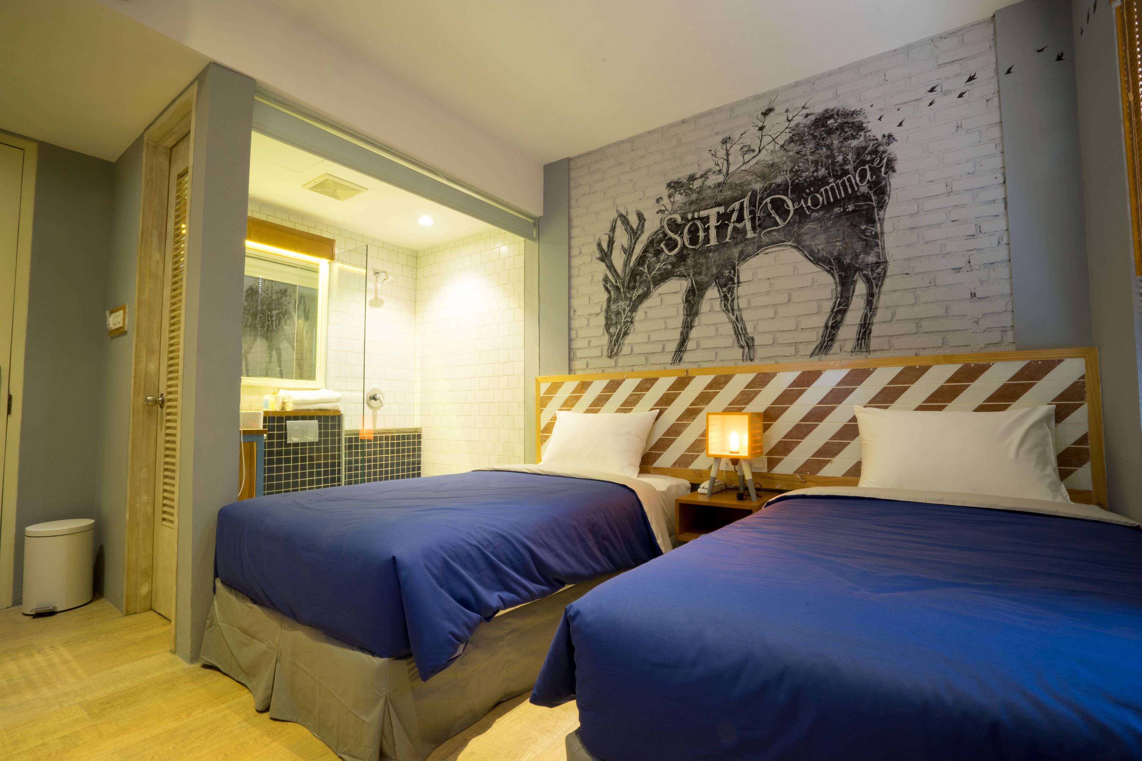 Quarto de hotel com duas camas, banheiro e um mural na parede.
