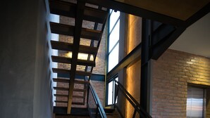 Eine Treppe mit Holzdielen und Metallgeländern, die zu einer Ebene mit einer Ziegelwand und einem kleinen Tisch mit einer Lampe führt.