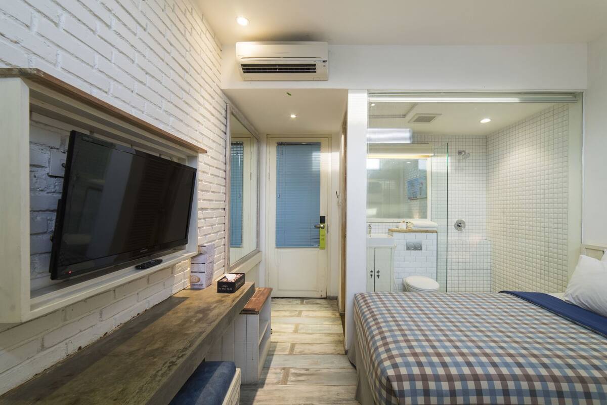 A modern hotel room with a television, a small seating area, a bathroom with a shower, and a bed.