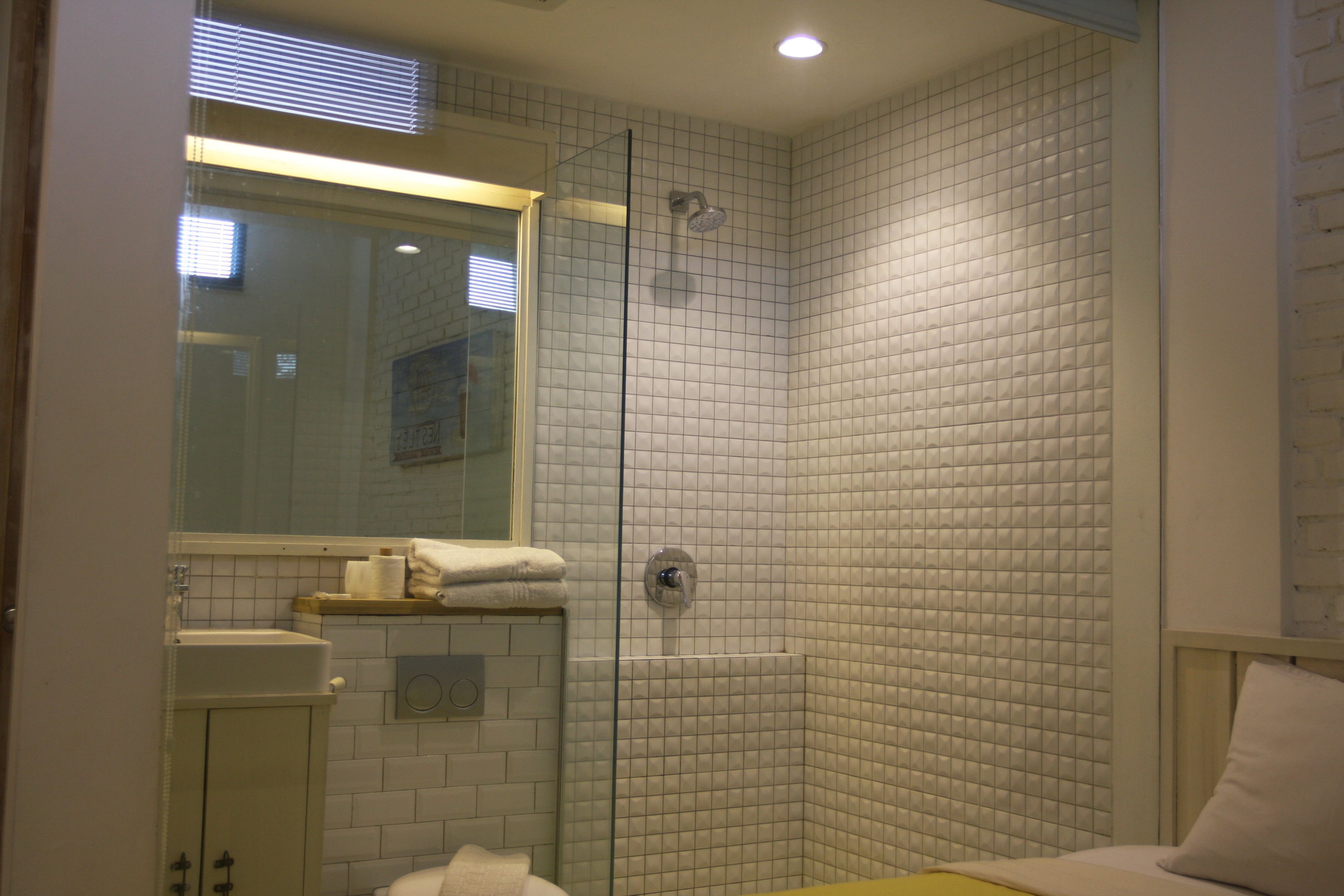 A bathroom with a glass-enclosed shower, white tiled walls, a sink, and a mirror.