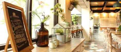 Interior de una cafetería con un pizarrón, una barra de madera y vistas al exterior.
