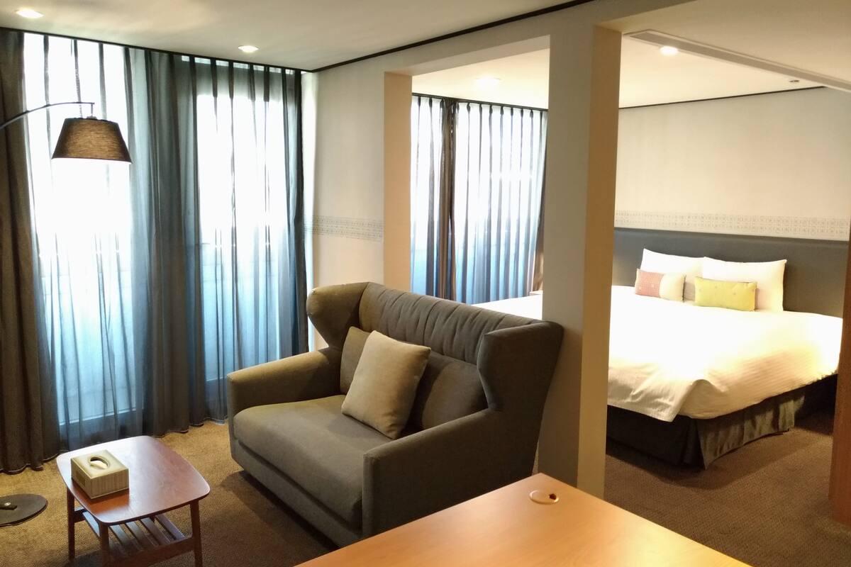 A hotel room with a sofa, a small table, a bed, and a lamp.