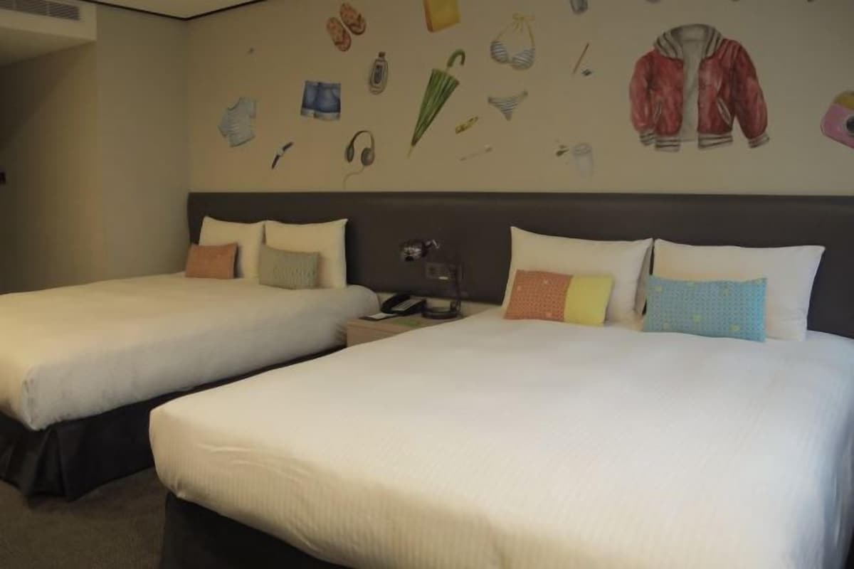 A hotel room with two beds, each with white linens and multiple pillows. The room has a large wall with various items like a jacket, headphones, and a phone.