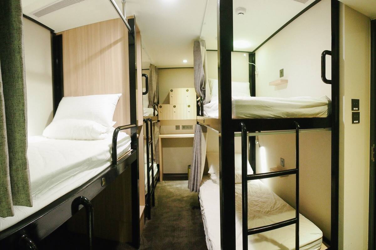 A narrow corridor with bunk beds on either side, a small desk area, and a door at the end.
