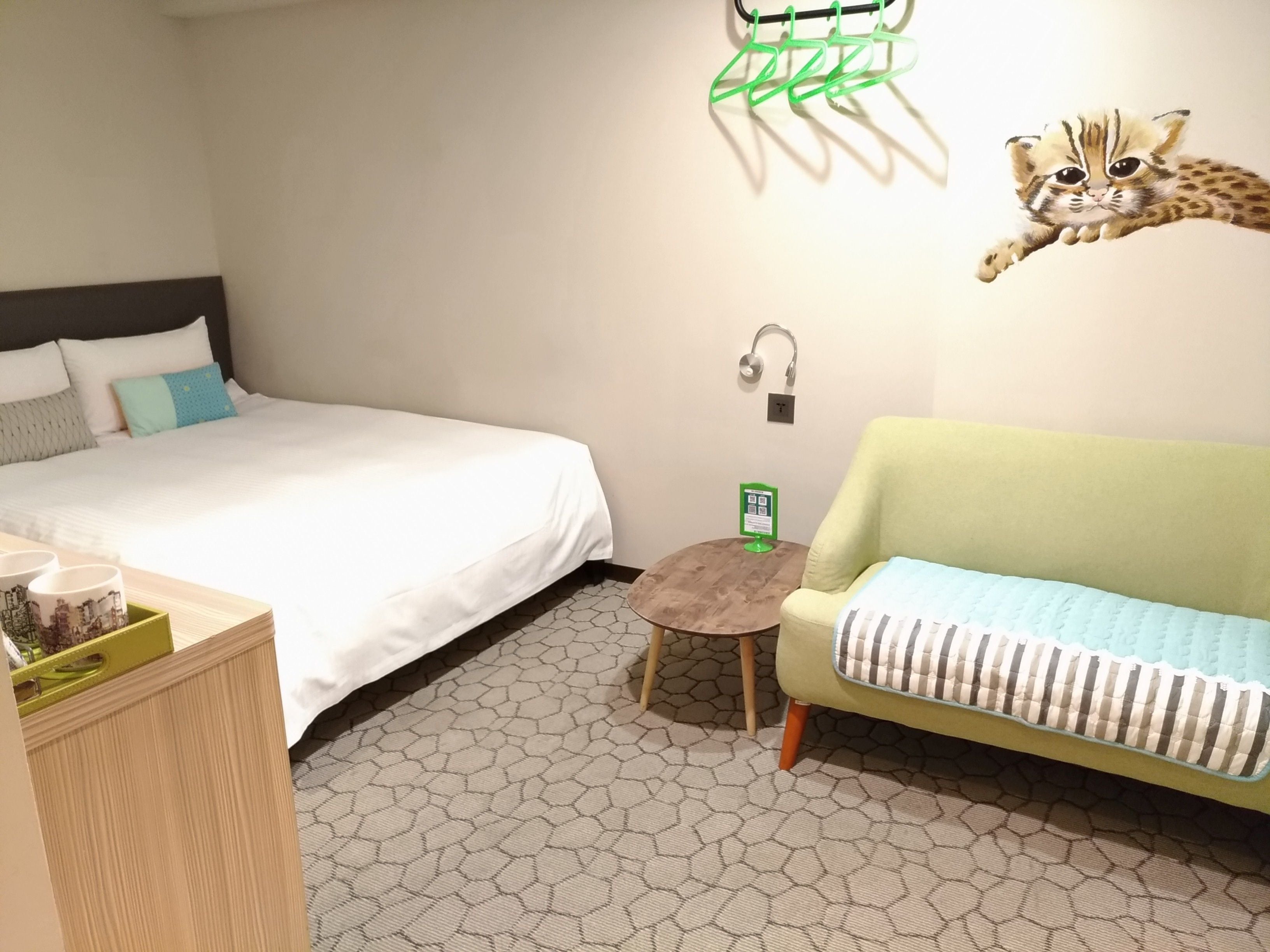 Une chambre d’hôtel avec un lit, un canapé, une petite table et une étagère fixée au mur.