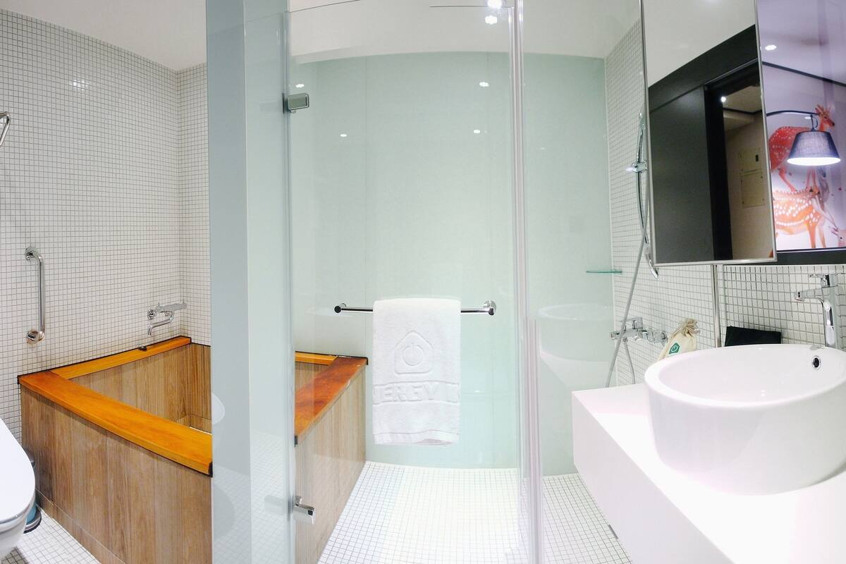 A modern bathroom with a glass shower enclosure, a wooden bathtub, a white sink, and a large mirror.