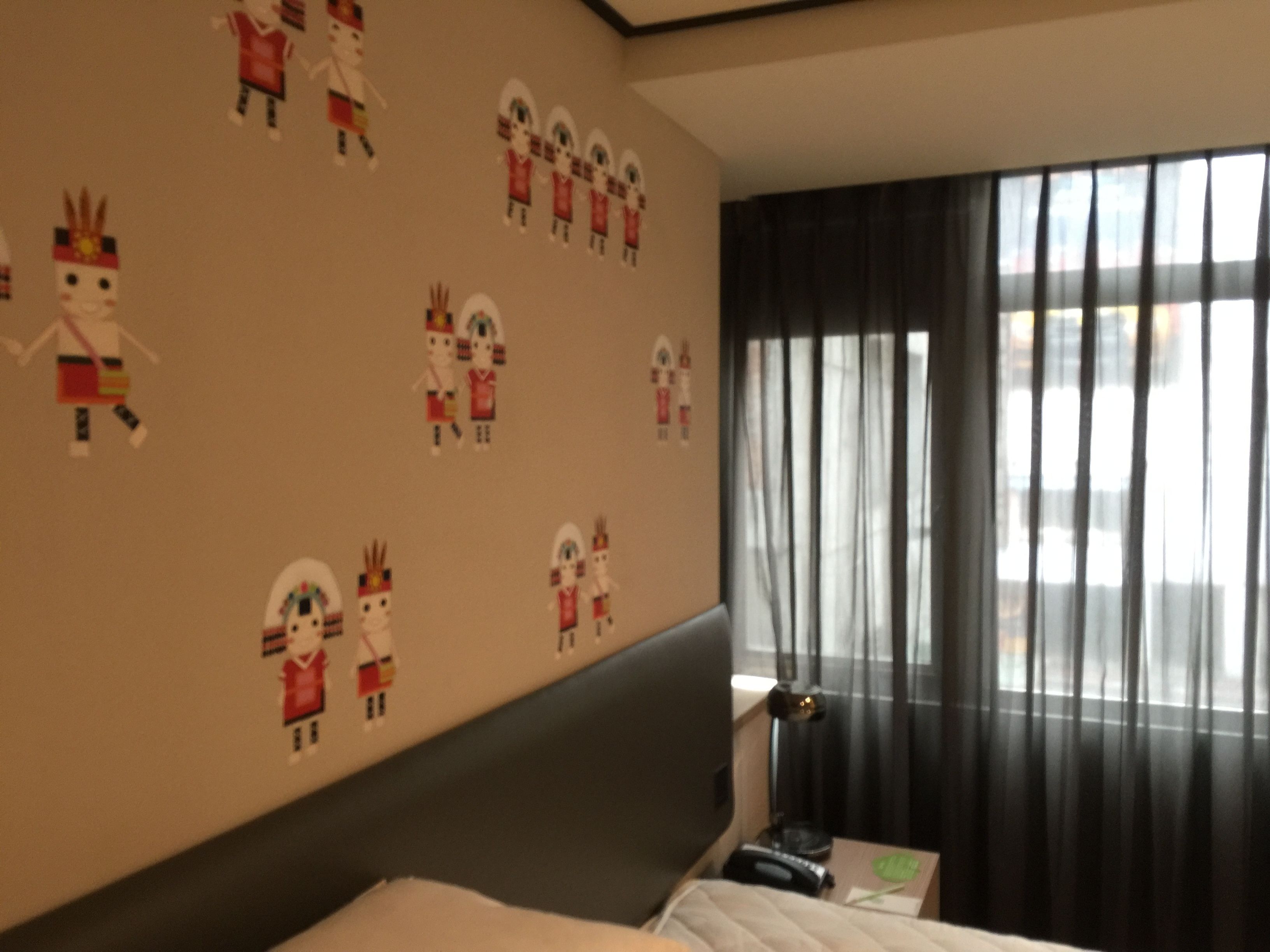 A hotel room with a bed, a nightstand, a lamp, and a window with curtains.