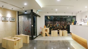 A hotel lobby with framed artwork on the walls, a reception desk, and a seating area with wooden stools. - Energy Inn (Taipei)